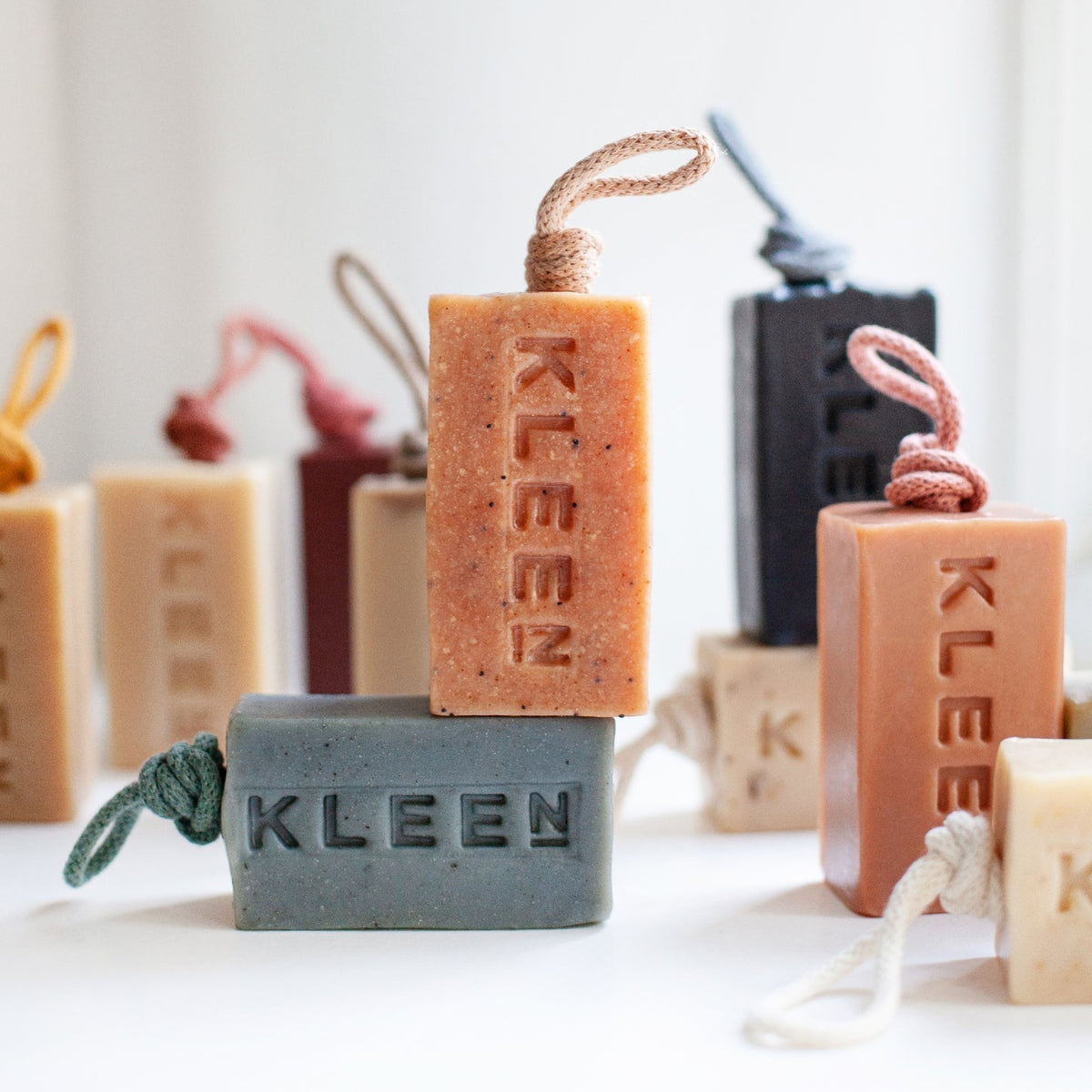 Stack of KLEEN handmade soaps on a rope in terracotta, sage, charcoal and cream with coloured cotton ropes