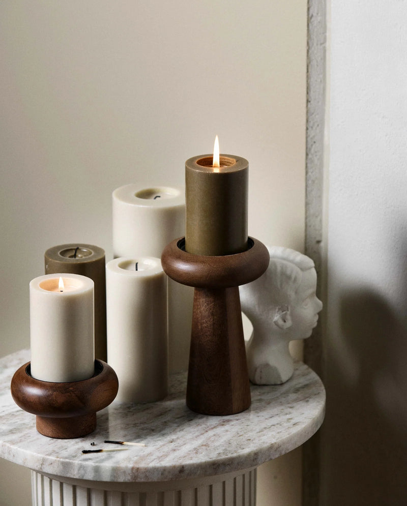 Beige pillar candle by Nordal styled on a wooden pedestal candle holder with a decorative bust
