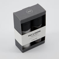 Salt and pepper shakers in a black and white packaging box on a light gray background