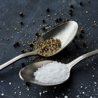 Two spoons with salt and pepper on a dark surface
