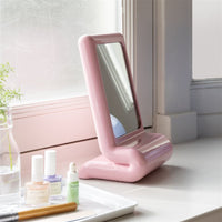 pink &k Amsterdam vanity mirror with chunky curved frame on a windowsill beside beauty items
