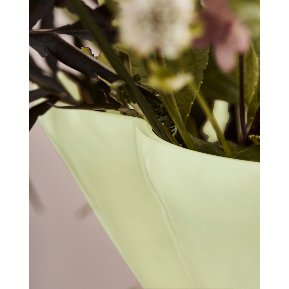 Close-up of the House Doctor Say vase rim with a wild bouquet of stems, leaves and seasonal blooms, soft lime glass adding a gentle pale chartreuse accent