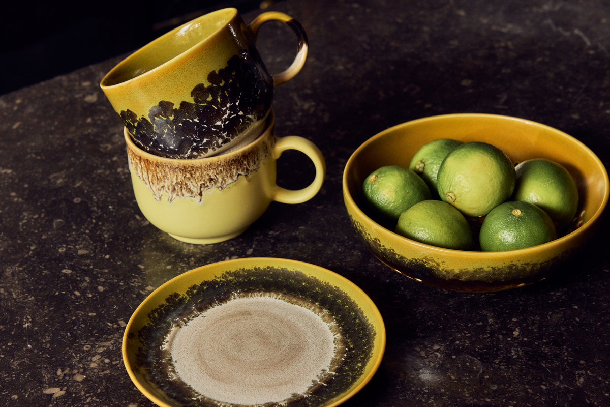 70s Ceramics tea mugs in Cravings stacked and styled on a dark counter alongside a matching bowl of limes and side plate
