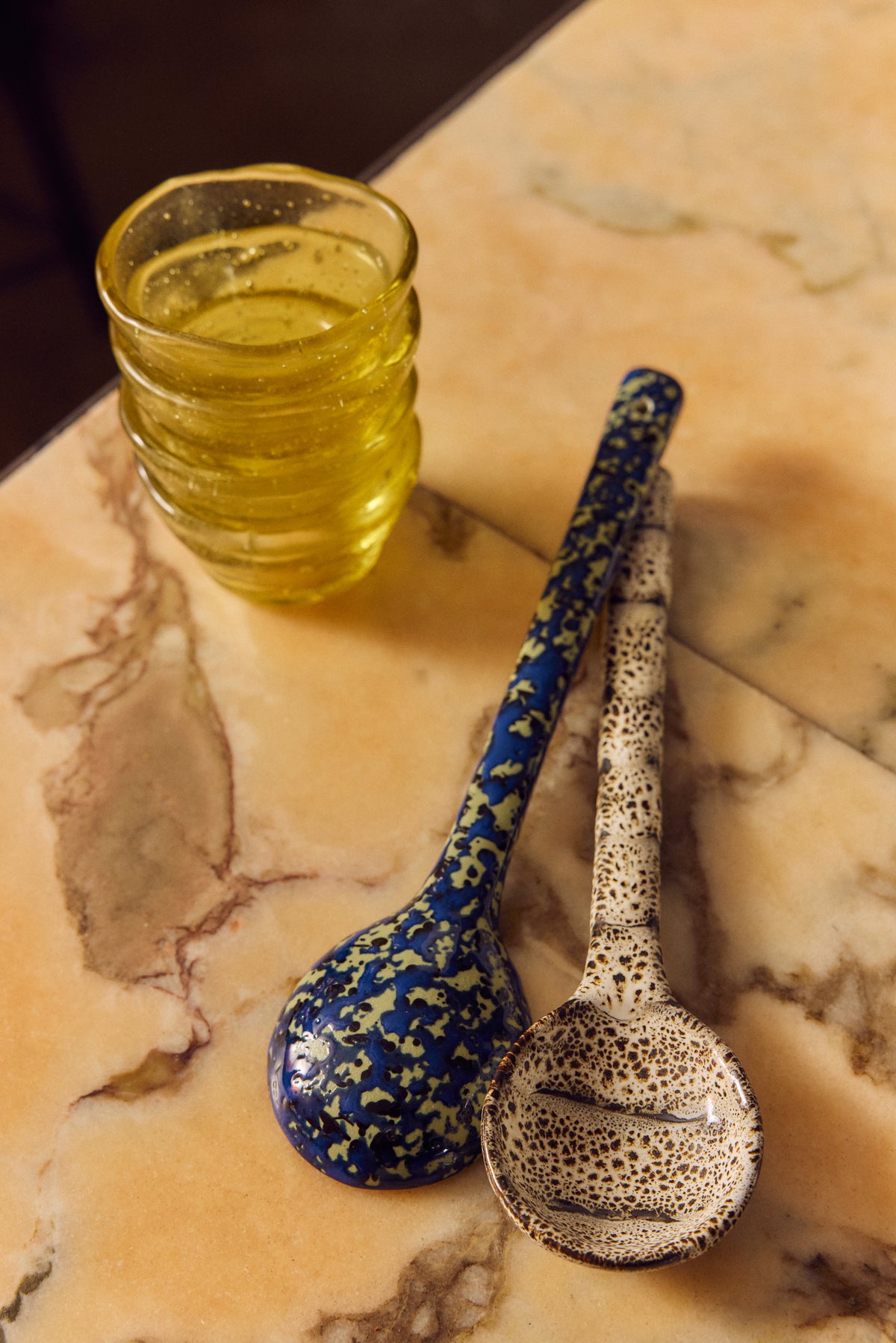 70s Ceramics serving spoons in Blues by HKLIVING styled on a marble table beside an amber glass tumbler