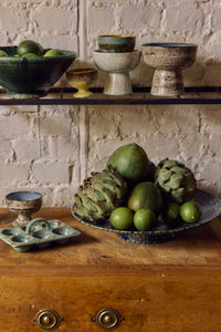 70s Ceramics Footed Fruit Bowl in Noise by HKLIVING on a wooden dresser, piled with artichokes, limes and green fruit