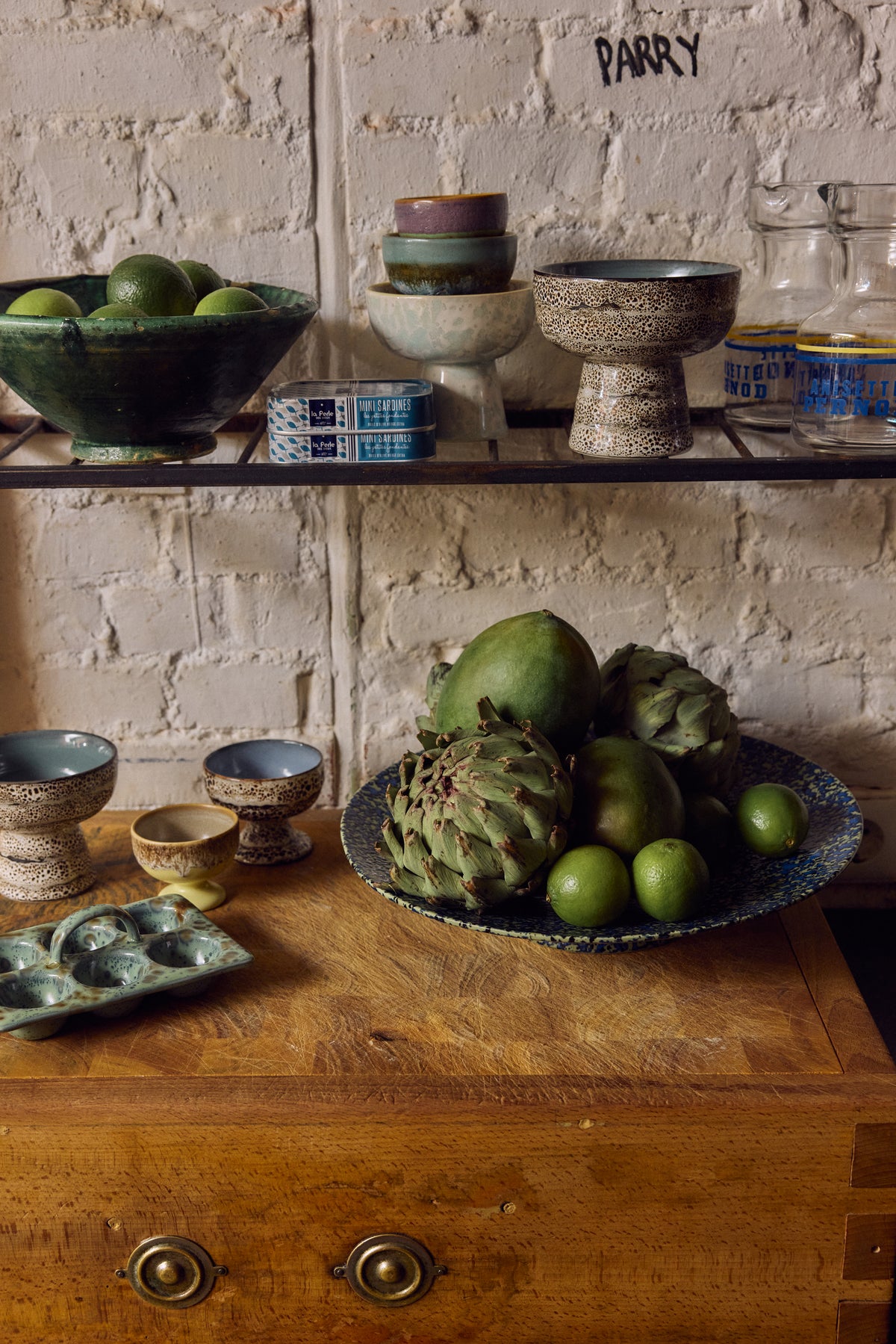 70s Ceramics tapas bowl on base in Brew displayed on an open shelf with artichokes, olives and other kitchen items