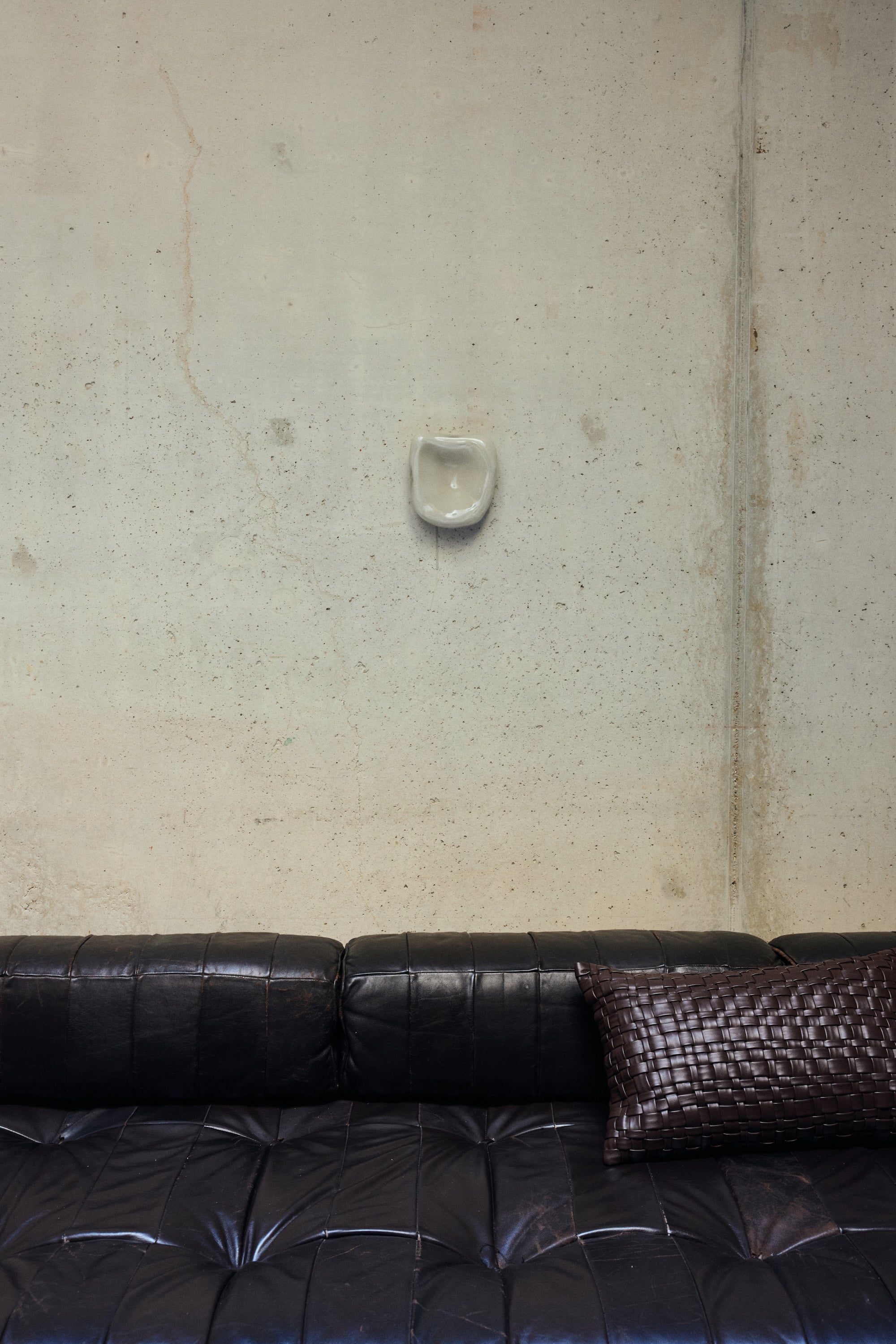 HKLIVING Dent Wall Sculpture in Overcast mounted on a concrete wall above a dark leather sofa