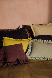 Lemongrass yellow linen cushion styled among burgundy and sage cushions on a bed
