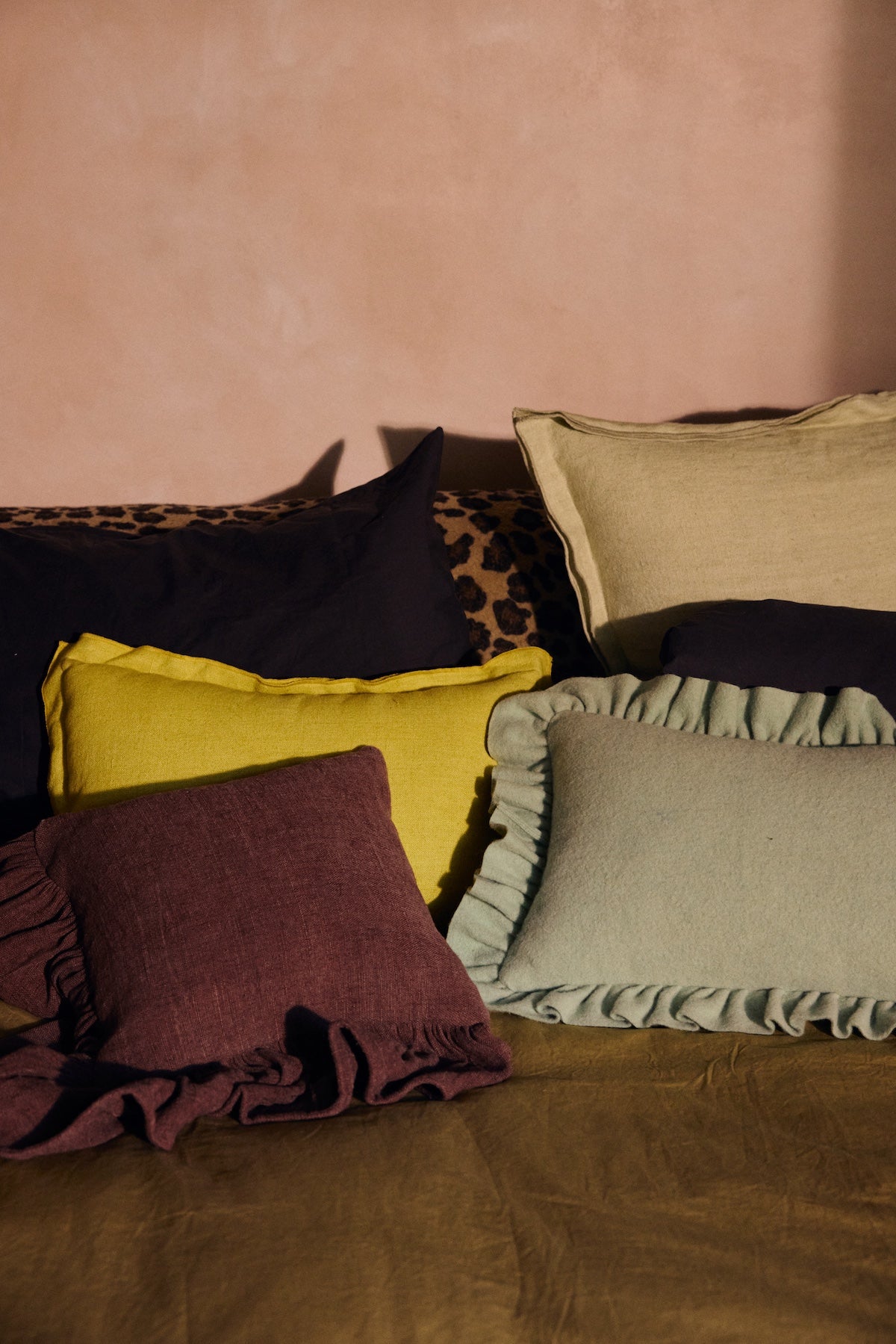 Lemongrass yellow linen cushion styled among burgundy and sage cushions on a bed