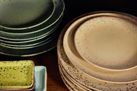 Close-up of stacked HKLIVING 70s Ceramics plates in sage green and sandy beige grit speckled glazes