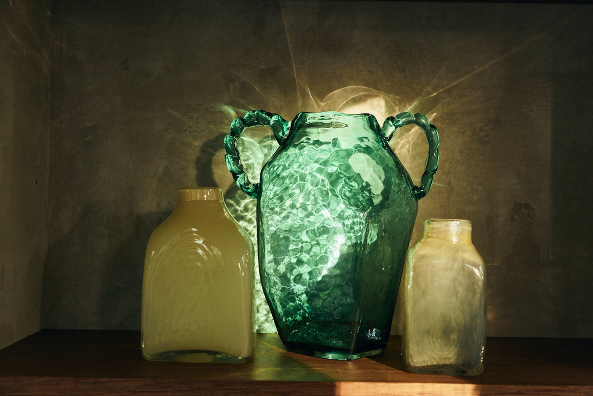 Green glass amphora hkliving vase styled on a shelf with smaller glass vessels, lit by sunlight