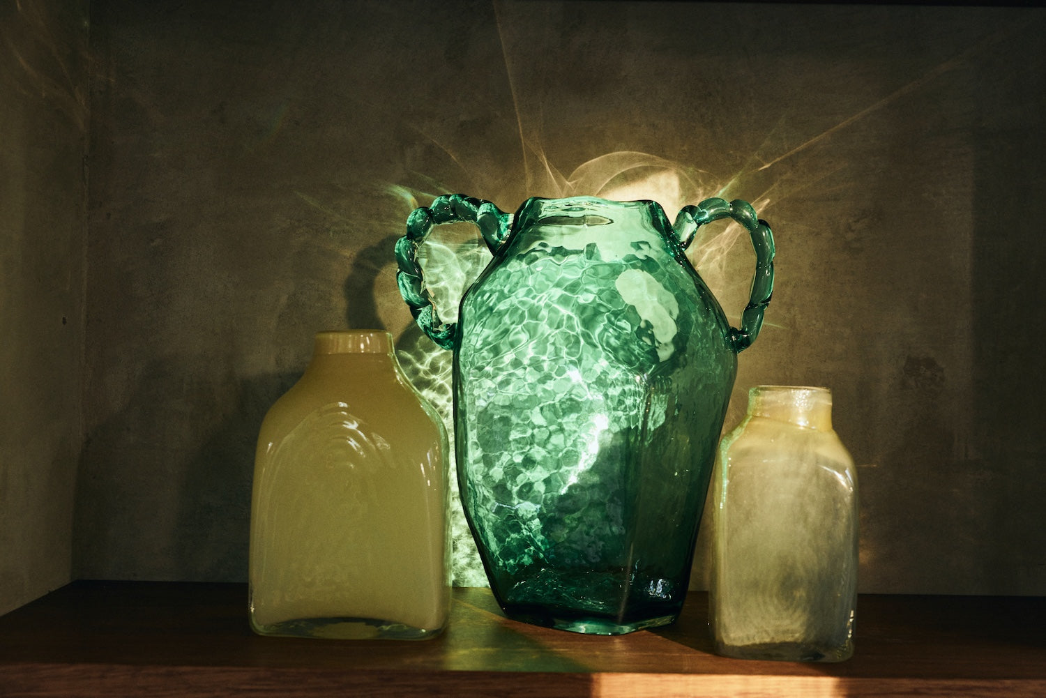 Green glass amphora hkliving vase styled on a shelf with smaller glass vessels, lit by sunlight