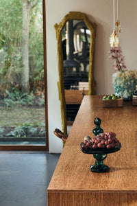 Emerald glass dessert stand styled with grapes on a wooden sideboard