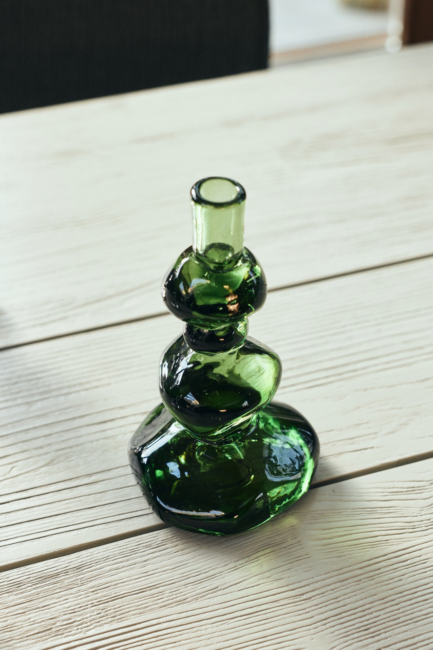 Emerald green glass candle holder with stacked sculptural design on pale wood table