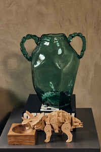 Green glass amphora hkliving vase with twisted handles styled on books beside a wooden dinosaur model