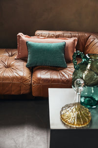 Deep sea turquoise hkliving velvet cushion styled with pink linen cushions on a leather sofa