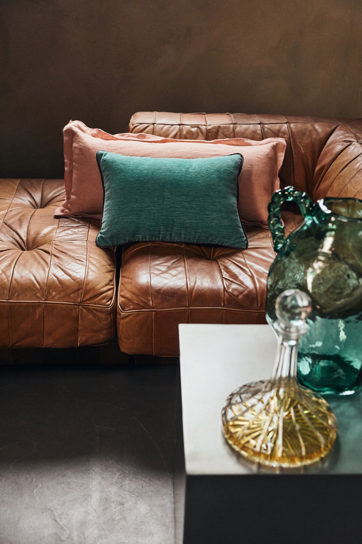 Deep sea turquoise hkliving velvet cushion styled with pink linen cushions on a leather sofa