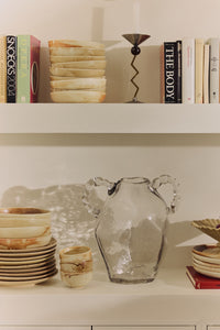 Clear glass amphora vase styled on a shelf among ceramics and books