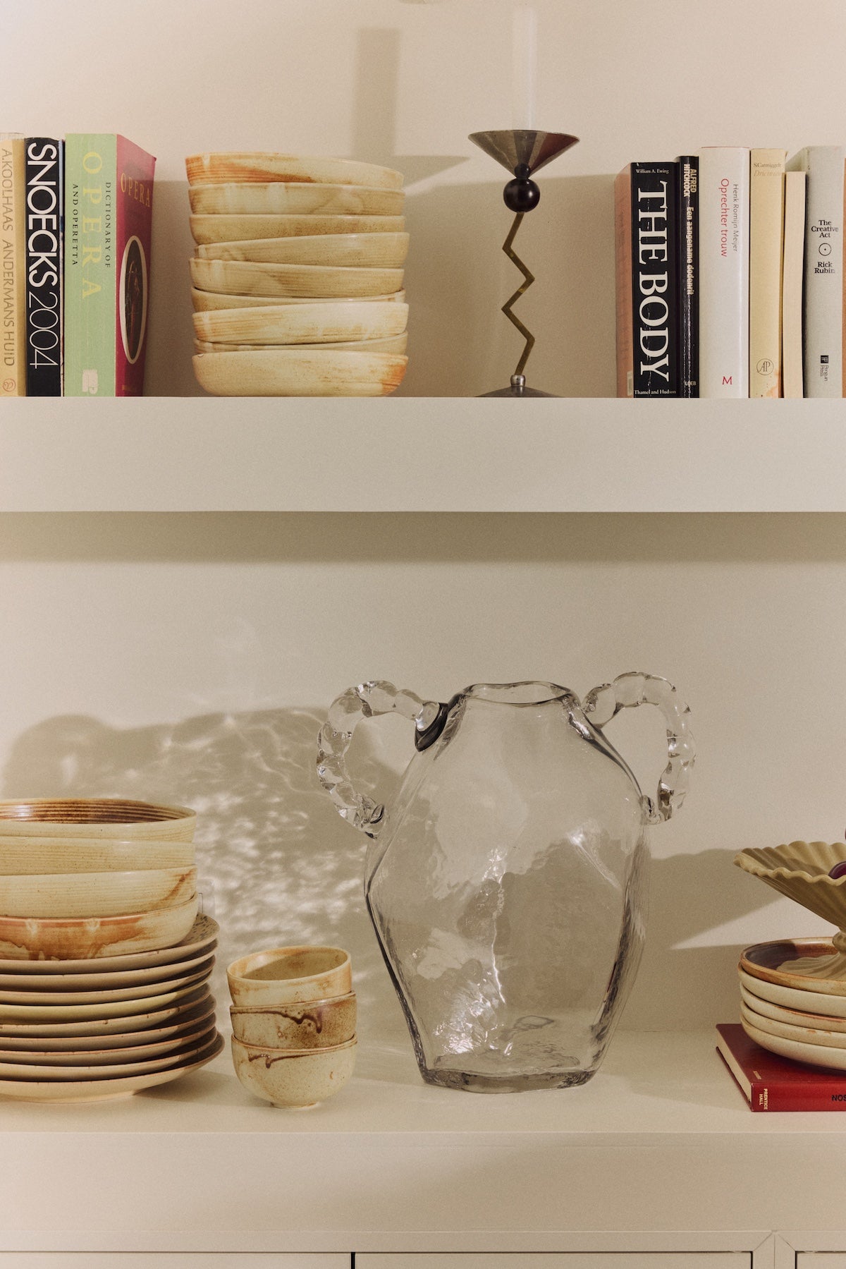Clear glass amphora vase styled on a shelf among ceramics and books