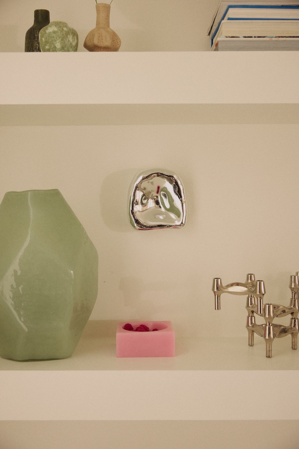The HKLIVING Pop Cube Small in Pink displayed on a shelf beside a green faceted vase, a silver dish and a pair of candle holders