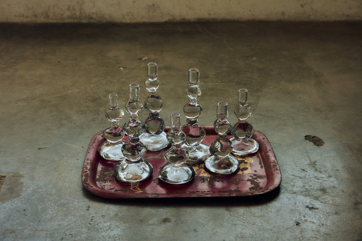 A group of clear Nienke Sikkema glass candle holders on a red tray on a concrete floor