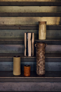 The Mono Vase, Sand/Black by HKLIVING displayed on metal steps alongside other tall ceramic vases in cream, brown and olive tones