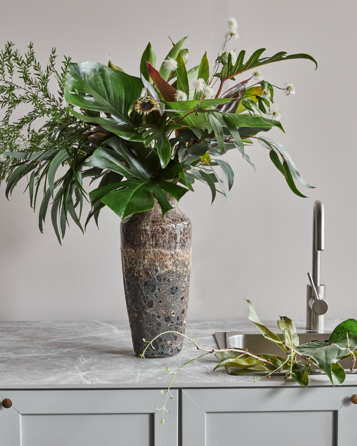 House Doctor Maya vase in a dark reactive glaze, styled with a tropical foliage arrangement on a kitchen counter