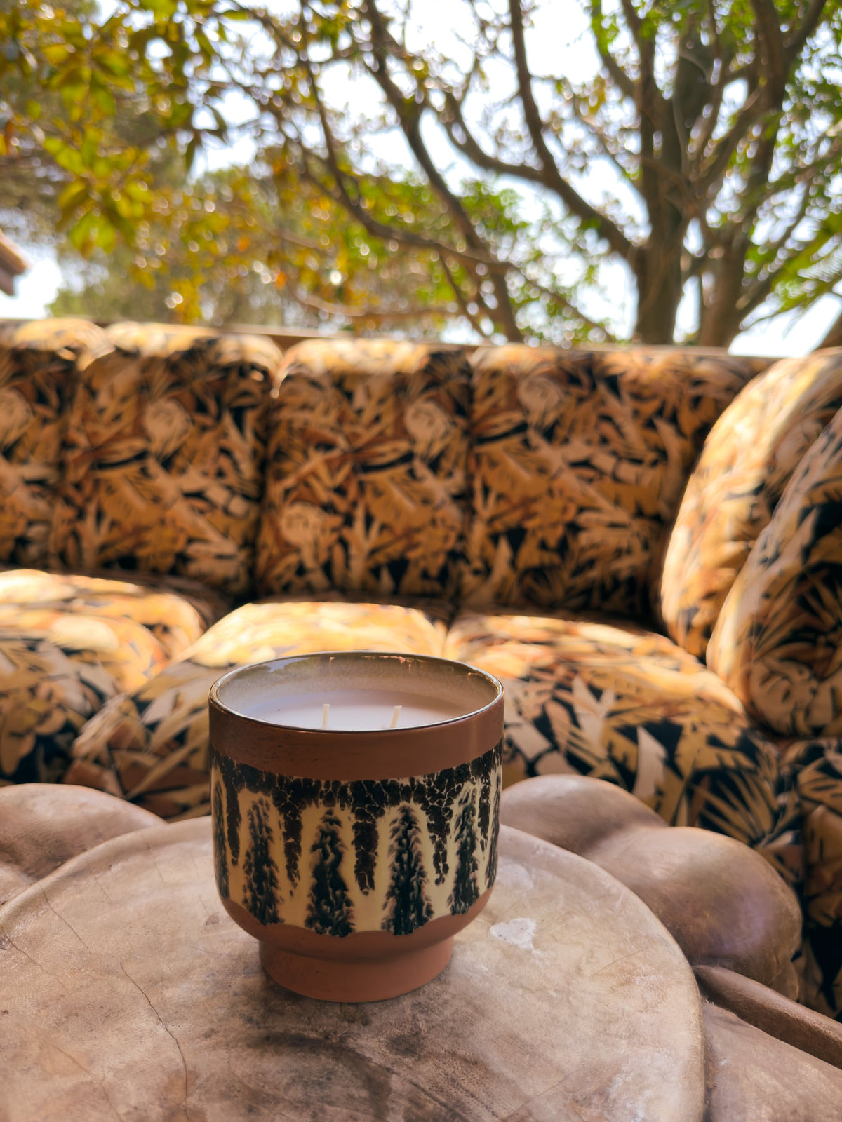 HKLIVING Kyoto scented candle on a round stone side table in front of a leopard print sofa outdoors