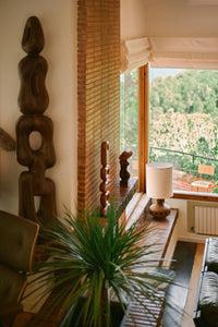 Living room with wooden sculptures, a lamp, and a view of greenery outside.