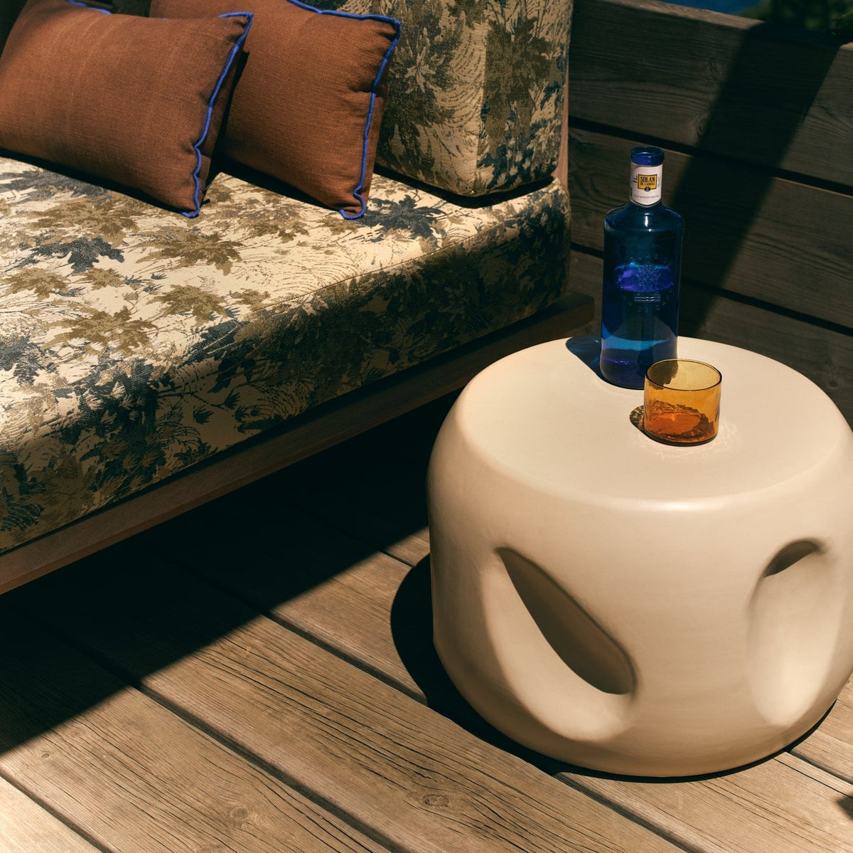 Cream HKLIVING Currents Shell side table on a sunlit wooden deck with a drink on top