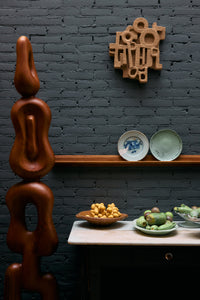 Dark brick wall with HKLIVING plates on a shelf, a tall carved wooden sculpture and a marble sideboard