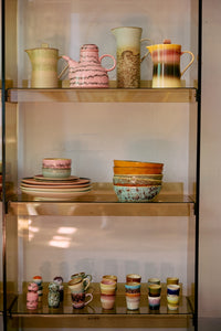 Close-up of four HKLIVING Futurism ristretto mugs stacked in pairs on a painted green shelf, in front of stoneware plates