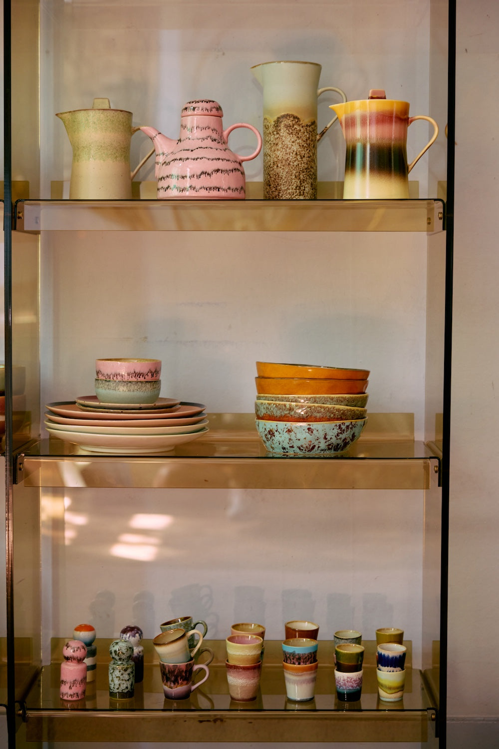 Close-up of four HKLIVING Futurism ristretto mugs stacked in pairs on a painted green shelf, in front of stoneware plates