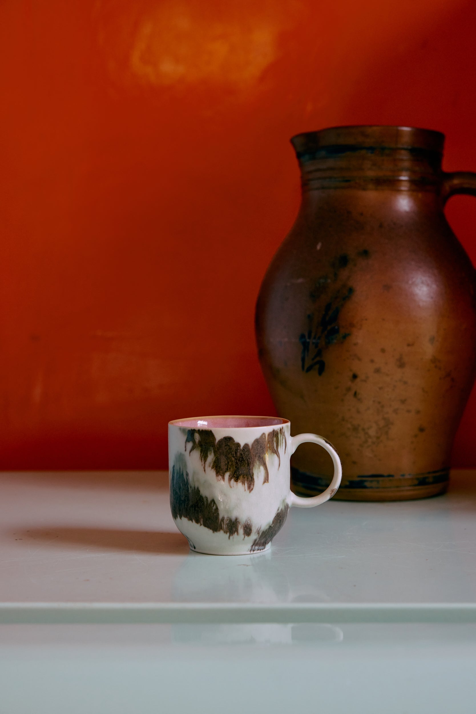 Ceramic mug and pitcher on a glass surface with an orange wall background