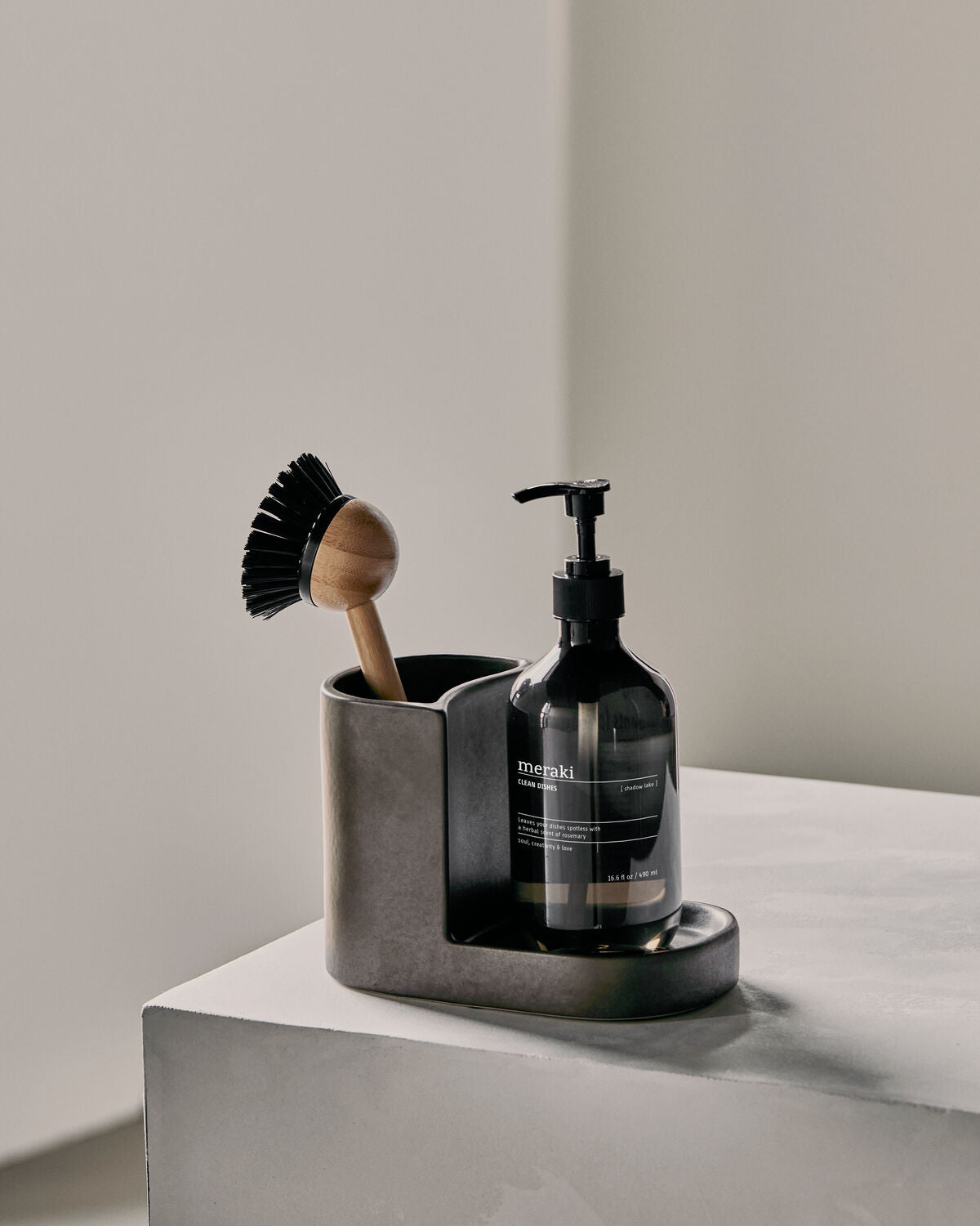 Regular Meraki Datura holder in dark grey with a dish brush and soap pump on a stone plinth