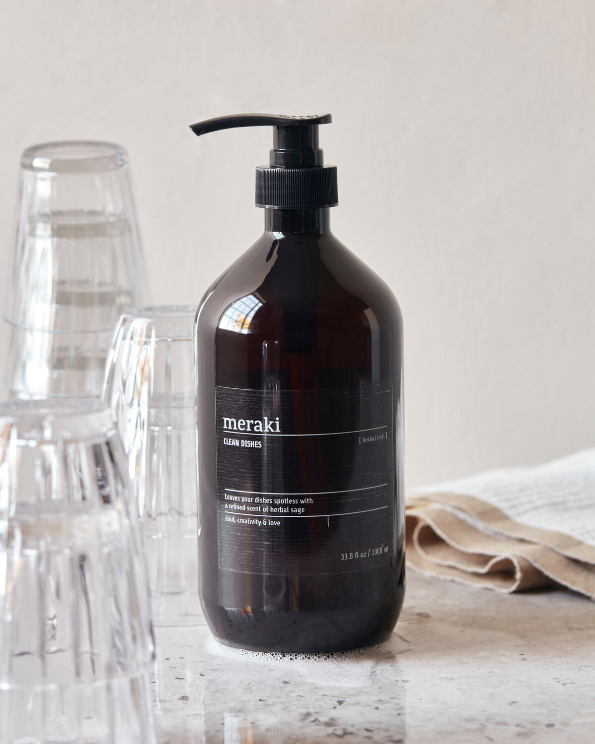 Meraki Herbal Nest dish wash bottle styled with glassware and linen, alternate view