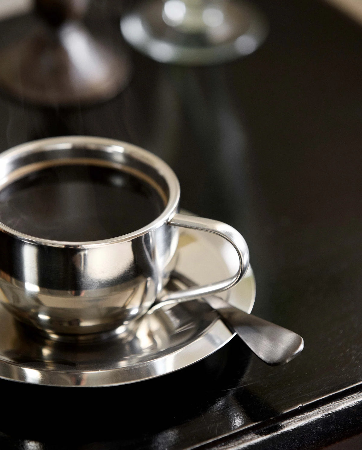 VIREA chrome cup and saucer by Nordal on a dark console table, styled with a candlestick and glass vase