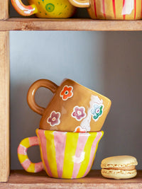 Addy cup brown with flowers stacked with other playful mugs on a shelf

