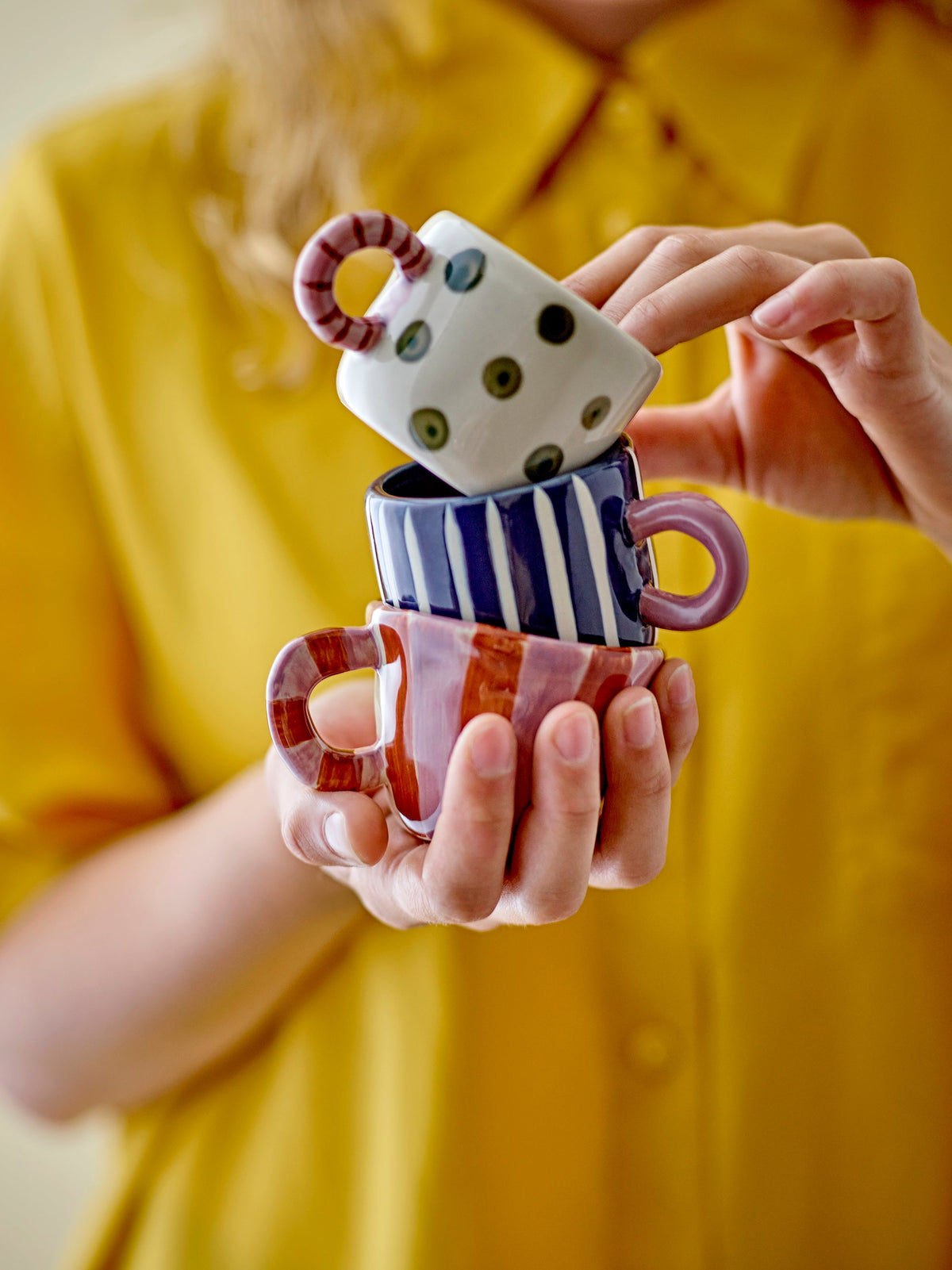 person holding stacked colourful bloomingville nini cups with playful hand-painted designs
