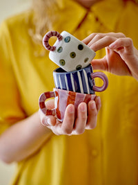 person holding stacked colourful bloomingville nini cups with playful hand-painted designs