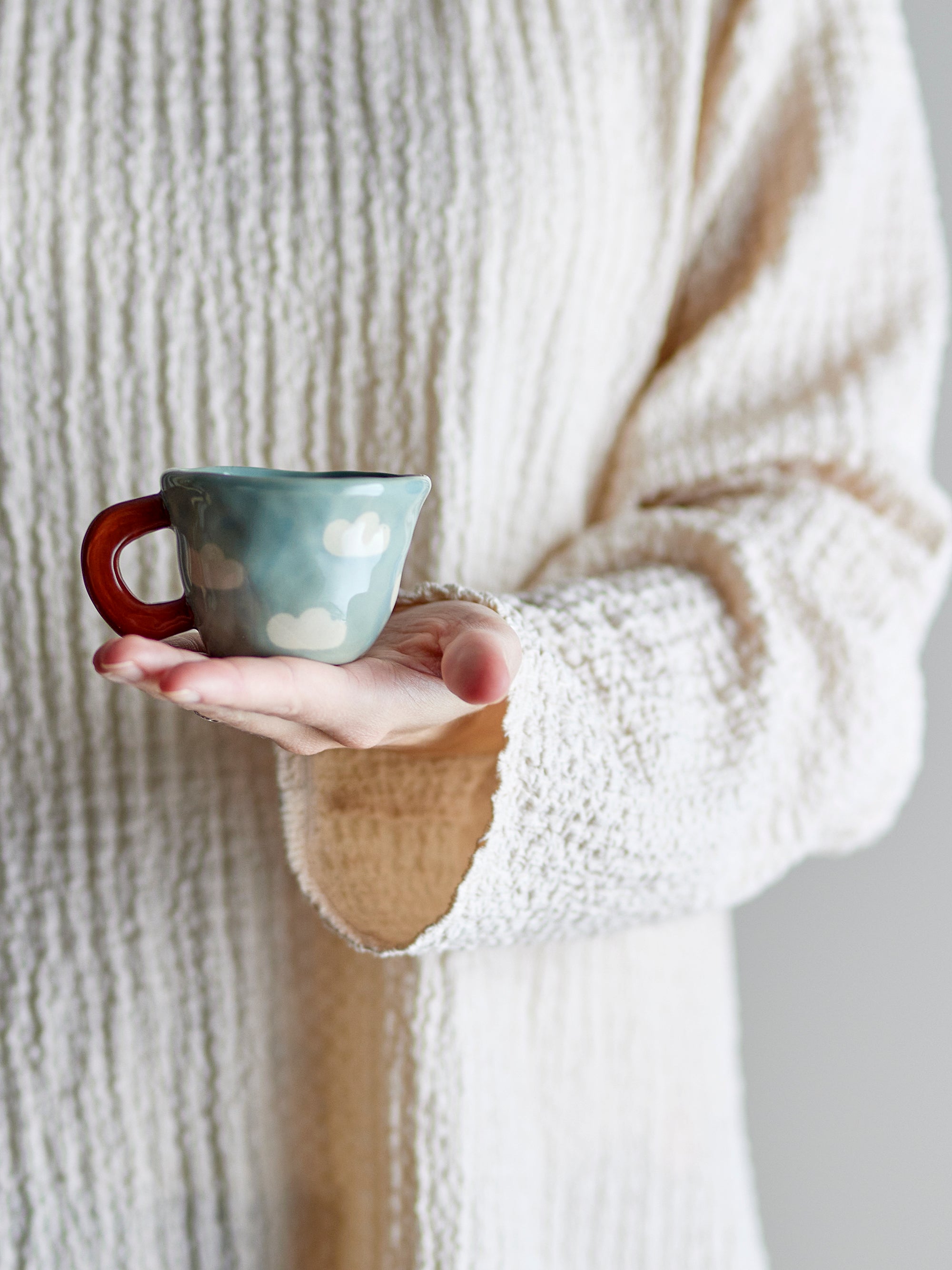 hand holding small blue nini cup with clouds and terracotta handle
