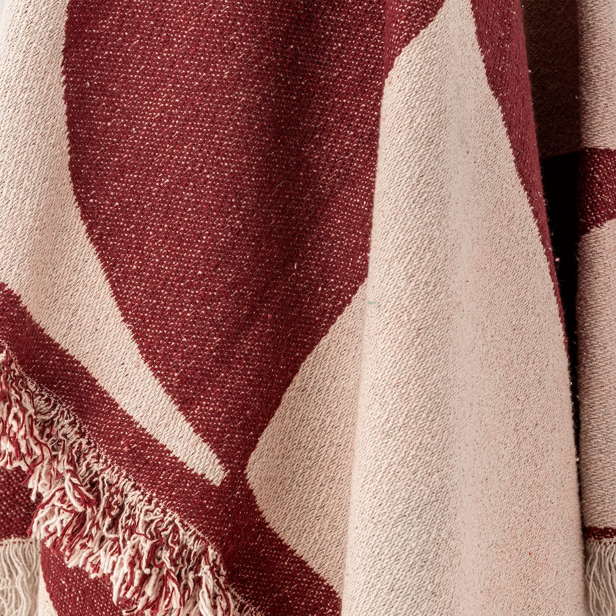 Close up of Olica throw fabric showing burgundy and cream abstract pattern detail