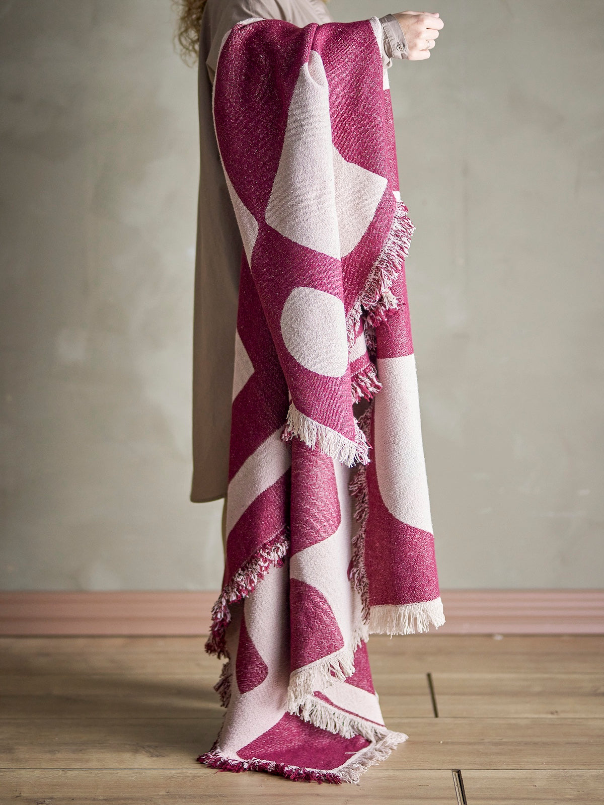 Olica burgundy throw draped over a model's arm showing abstract pattern and fringe