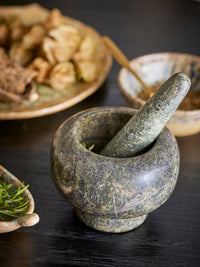 Mortar and pestle with herbs on a dark surface