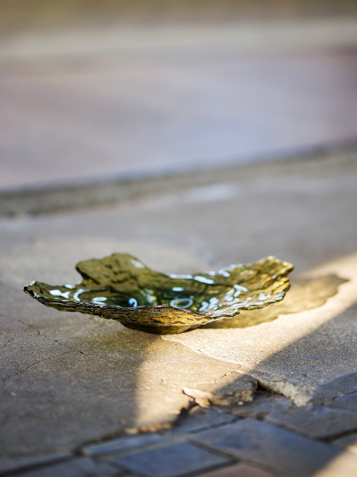 Aiku olive green glass bowl styled on a stone floor beside marble side tables