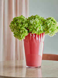 Janine coral red glass vase filled with green hydrangeas on a wooden table