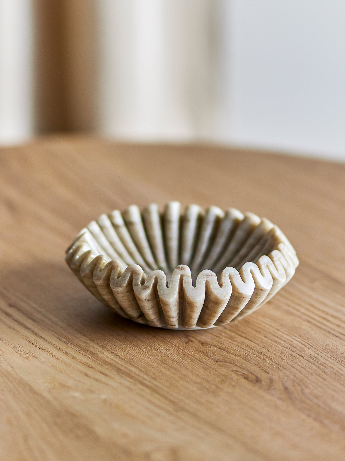 Harmonia beige marble bowl on a light oak table with a soft blurred window behind