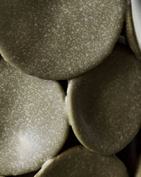 Extreme close-up of the speckled matte khaki glaze and overlapping ceramic discs on the handmade House Doctor Dot vase, tactile ceramic detail