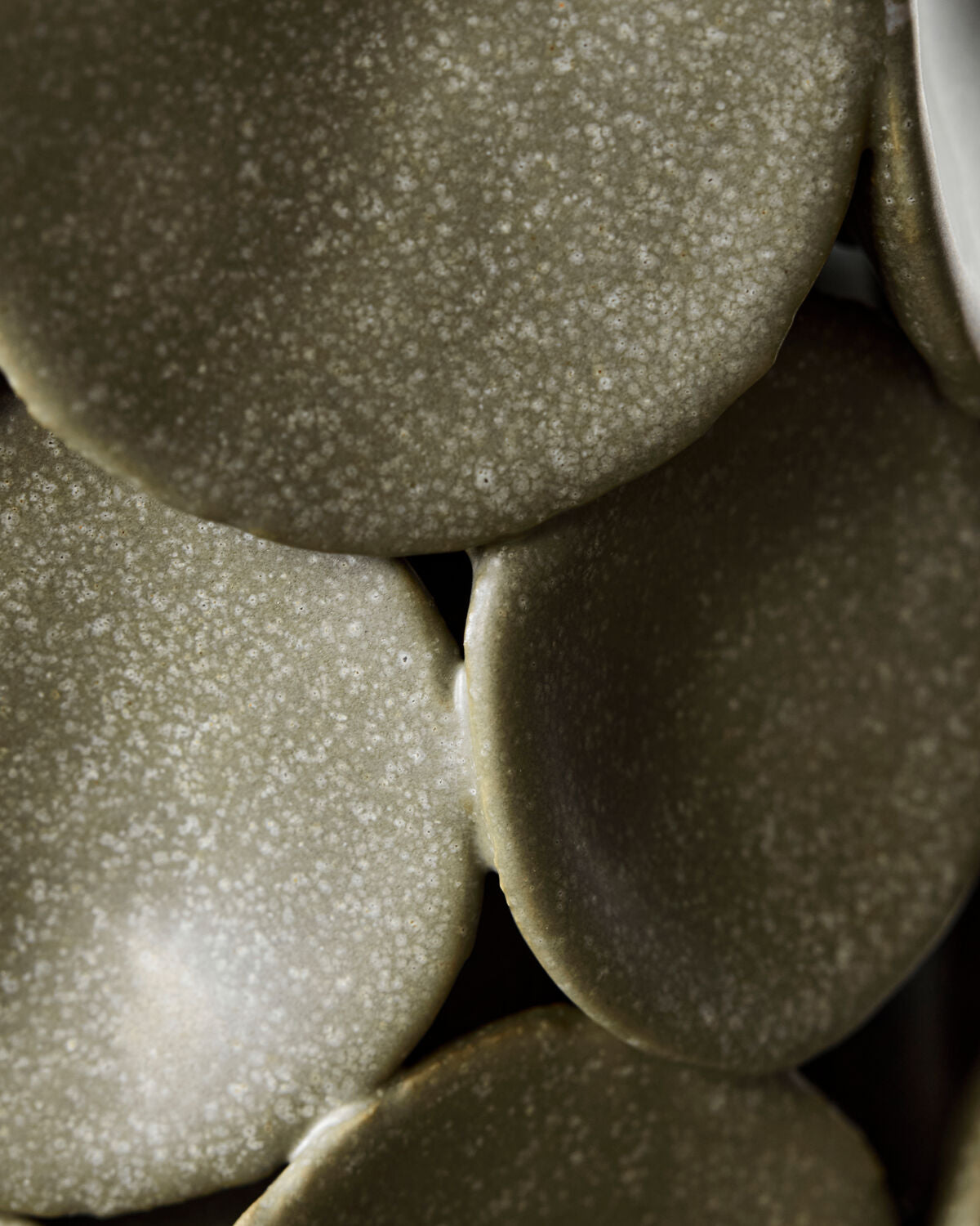 Extreme close-up of the speckled matte khaki glaze and overlapping ceramic discs on the handmade House Doctor Dot vase, tactile ceramic detail