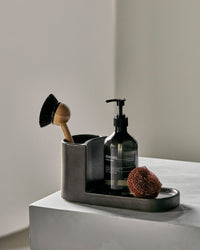 Meraki Datura brush and soap holder in dark grey stoneware, styled with a dish brush, soap bottle and scourer